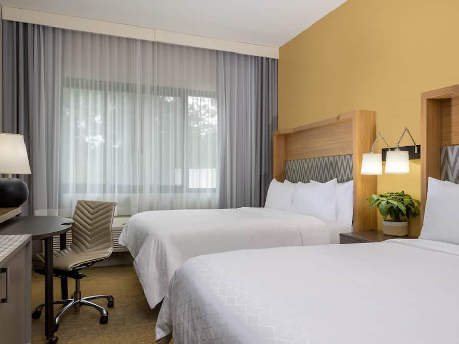 Une chambre d’hôtel avec deux lits, un bureau, une chaise, une télévision et une lampe.