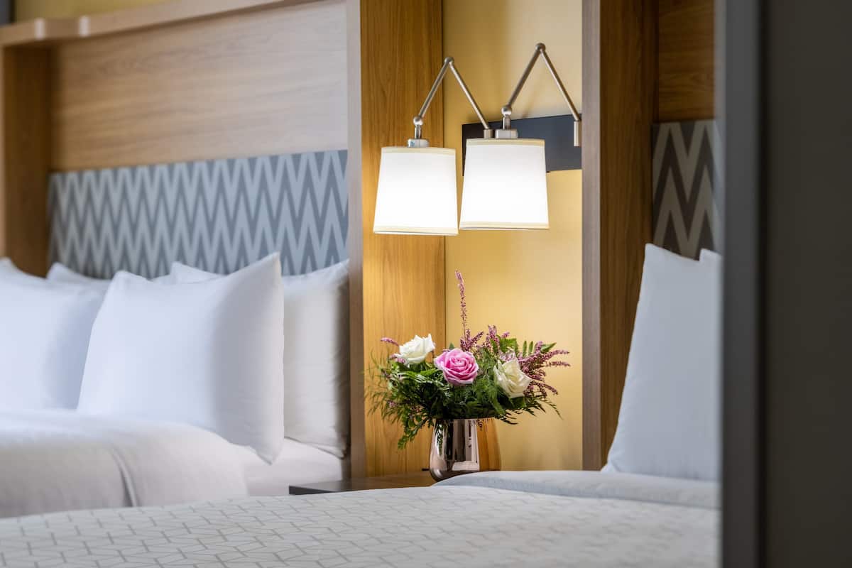 Een hotelkamer met een bed, een nachtkastje met een bloevas en twee wandlampen.