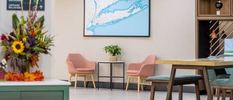 Una zona de recepción con un mapa en la pared, dos sillones rosados, una mesita con una planta y un escritorio de madera con sillas.