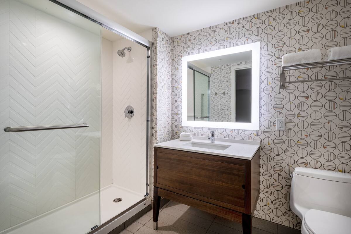 Een moderne badkamer met een glazen douchecabine, een houten wastafelmeubel en een behang met patroon.