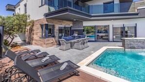 Una casa moderna de dos pisos con piscina, mobiliario exterior y zona de patio.