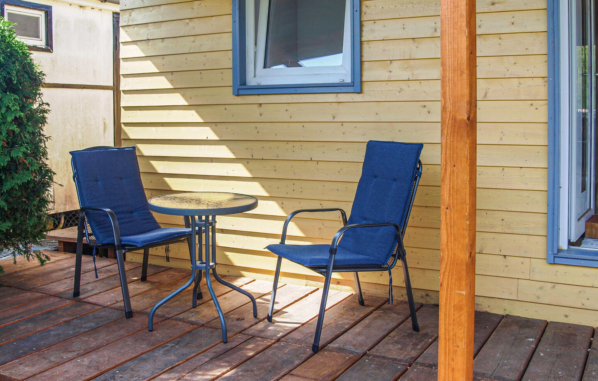 A wooden deck with two blue chairs and a small round table.