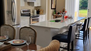 Una cocina moderna con armarios blancos, un refrigerador de acero inoxidable, horno empotrado y una isla grande con asientos tipo barra.