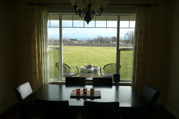 Een eettafel met vier stoelen, een kroonluchter en uitzicht op een grasveld door een groot raam.