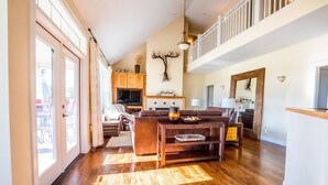 A spacious living room with a wooden floor, a fireplace, a dining area, and a view of the outdoors.