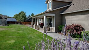 A two-story house with a covered patio, a well-maintained lawn, and flowering plants.