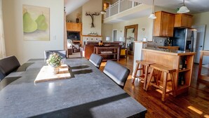 A spacious living area with a dining table, seating, a kitchen with wooden cabinets, and a staircase leading to an upper level.