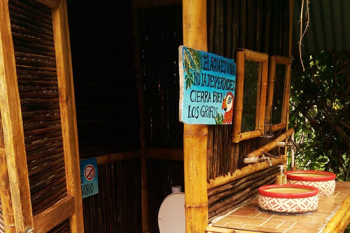 A rustic bathroom with a bamboo structure, a toilet, and a sign in Spanish.