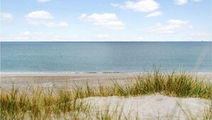 Una spiaggia con dune sabbiose e erba in primo piano, che si apre su un mare calmo sotto un cielo sereno.