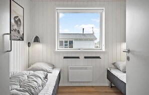 A small, well-lit bedroom with two beds, a window with a view of a house, and a radiator.