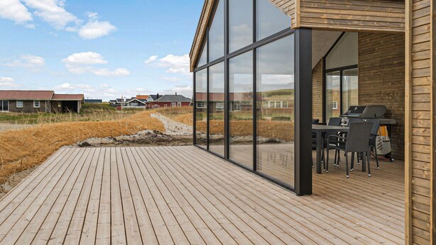 Un terrazzo in legno con veranda in vetro, un barbecue e sedute da esterno.