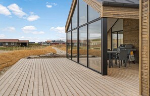 Un terrazzo in legno con veranda in vetro, un barbecue e sedute da esterno.