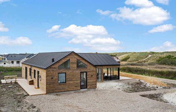 A modern wooden house with a sloped roof, large windows, and a covered porch area.