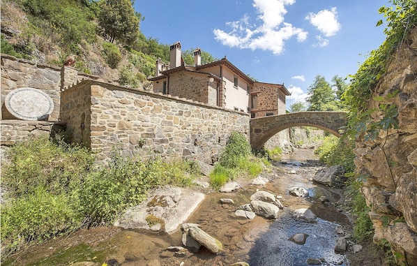 A stone building with a stone bridge over a stream, surrounded by greenery. - Cozy home in Greve in Chianti with sauna (Greve in Chianti)