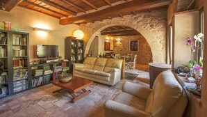 A cozy living room with a stone archway, a leather sofa, a coffee table, and a bookshelf filled with books and DVDs. - Cozy home in Greve in Chianti with sauna (Greve in Chianti)