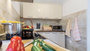 A modern kitchen with white cabinets, a gas stove, a microwave, and a variety of fresh vegetables on the counter. - Lovely home in Krnica (Krnica)