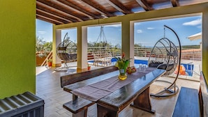A covered outdoor seating area with a wooden table, two chairs, and a hanging chair. - Lovely home in Krnica (Krnica)