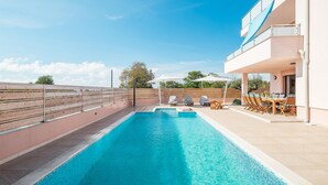 A swimming pool with lounge chairs and umbrellas, a covered outdoor dining area, and a view of the surrounding landscape.