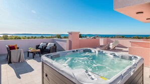 A rooftop terrace with a hot tub, seating area, and a view of the sea.