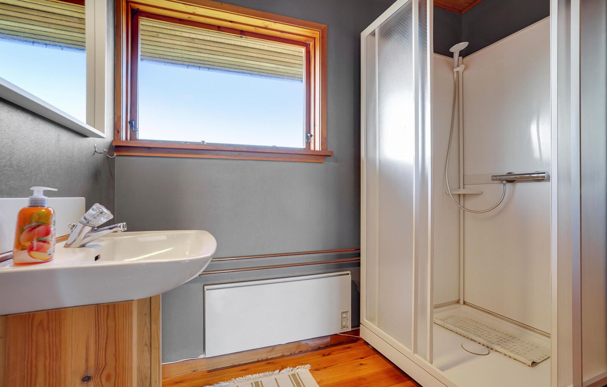 A bathroom with a white sink, wooden cabinet, and a glass shower enclosure.