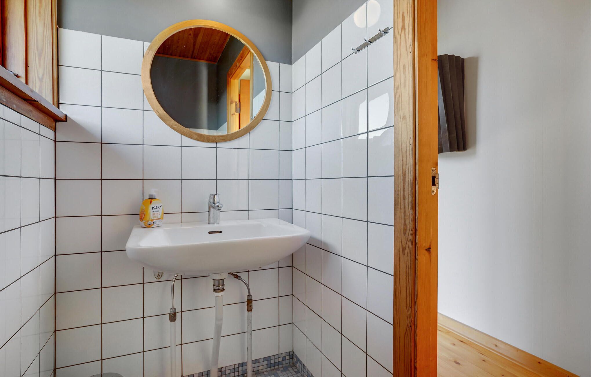 A bathroom with a white sink, a wooden-framed mirror, and a tiled wall.
