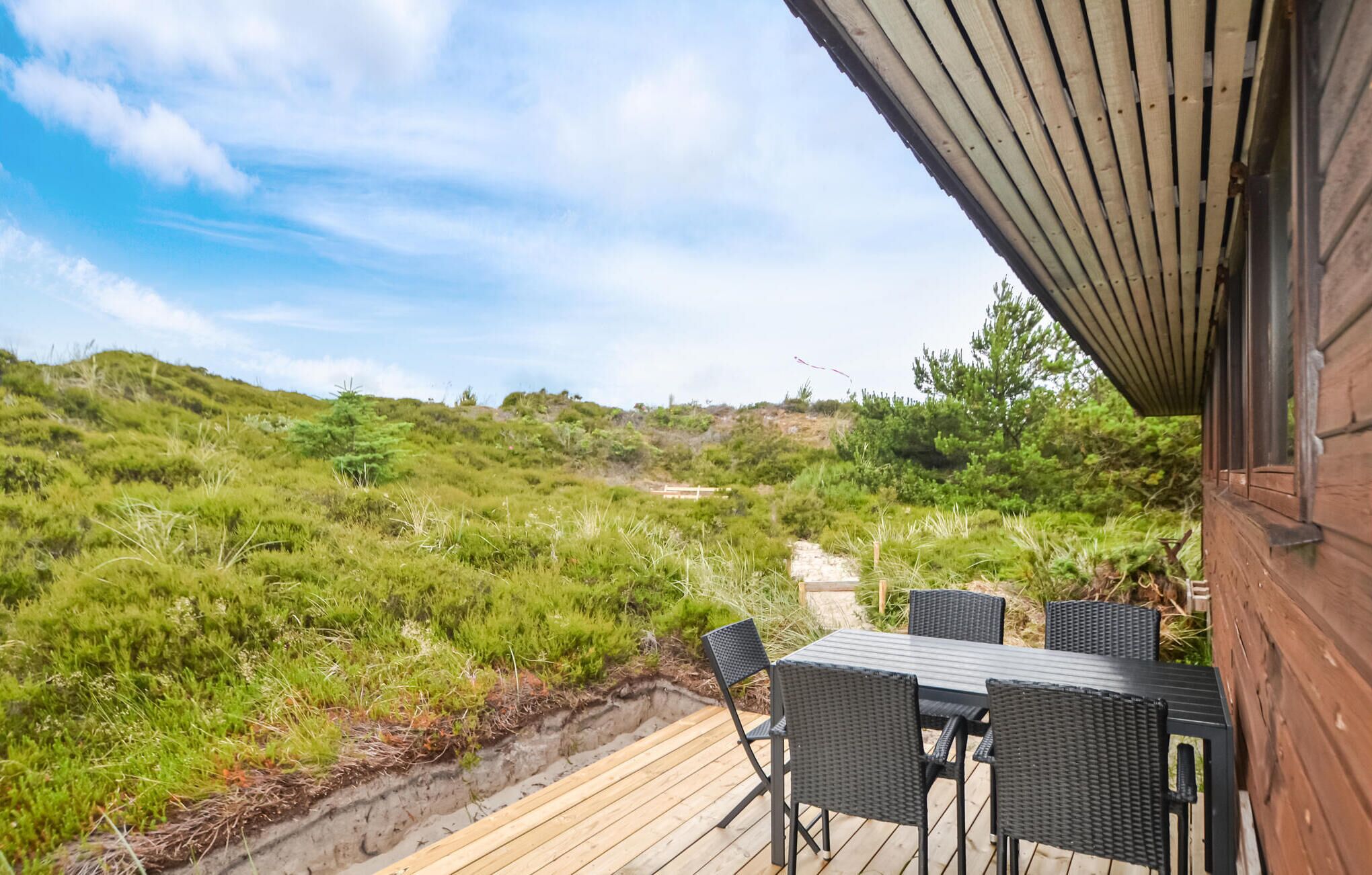 Eine Holzterrasse mit Gartenmöbeln, mit Blick auf eine grüne Landschaft mit Weg und Bäumen.