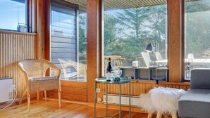 A cozy room with wooden walls, a wicker chair, a round table with a bottle, glasses, and a lamp.