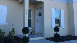 A two-story residential building with a beige exterior, white shutters, and a front porch. - It’s only 15 minutes drive to Disney World and the amazing outlets in Orlando (Kissimmee)