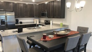 A modern kitchen with dark cabinets, stainless steel appliances, a granite countertop, and a dining area with a dark table and gray chairs. - It’s only 15 minutes drive to Disney World and the amazing outlets in Orlando (Kissimmee)