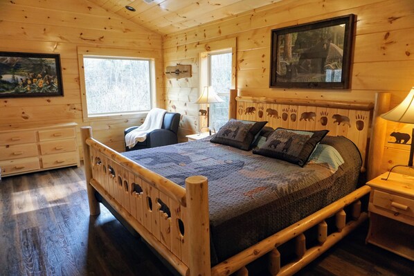A wooden cabin bedroom with a bed, dresser, and two windows.