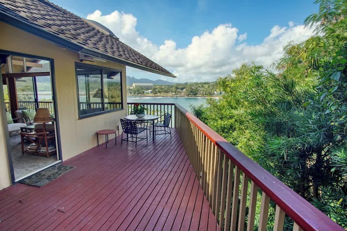 A wooden deck with a table and chairs, overlooking a body of water and greenery.
