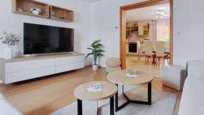 Una sala moderna con televisor de pantalla plana, un comedor con mesa y sillas, y una cocina visible a través de un vano abierto.