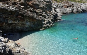 A rocky coastline with clear turquoise water and a person swimming.