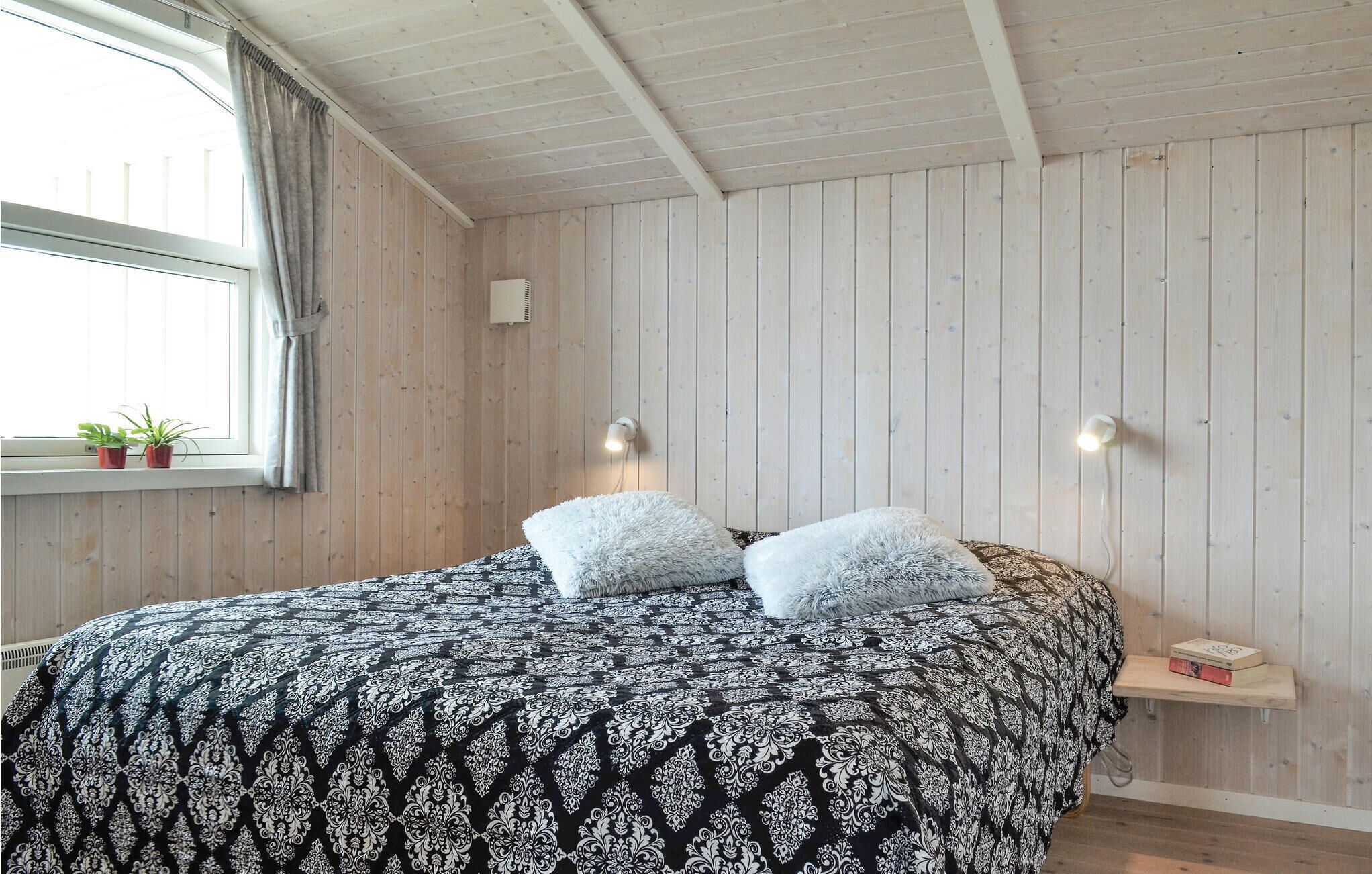 Una camera da letto con un letto, due lampade ai comodini, una finestra con tende e una piccola libreria.