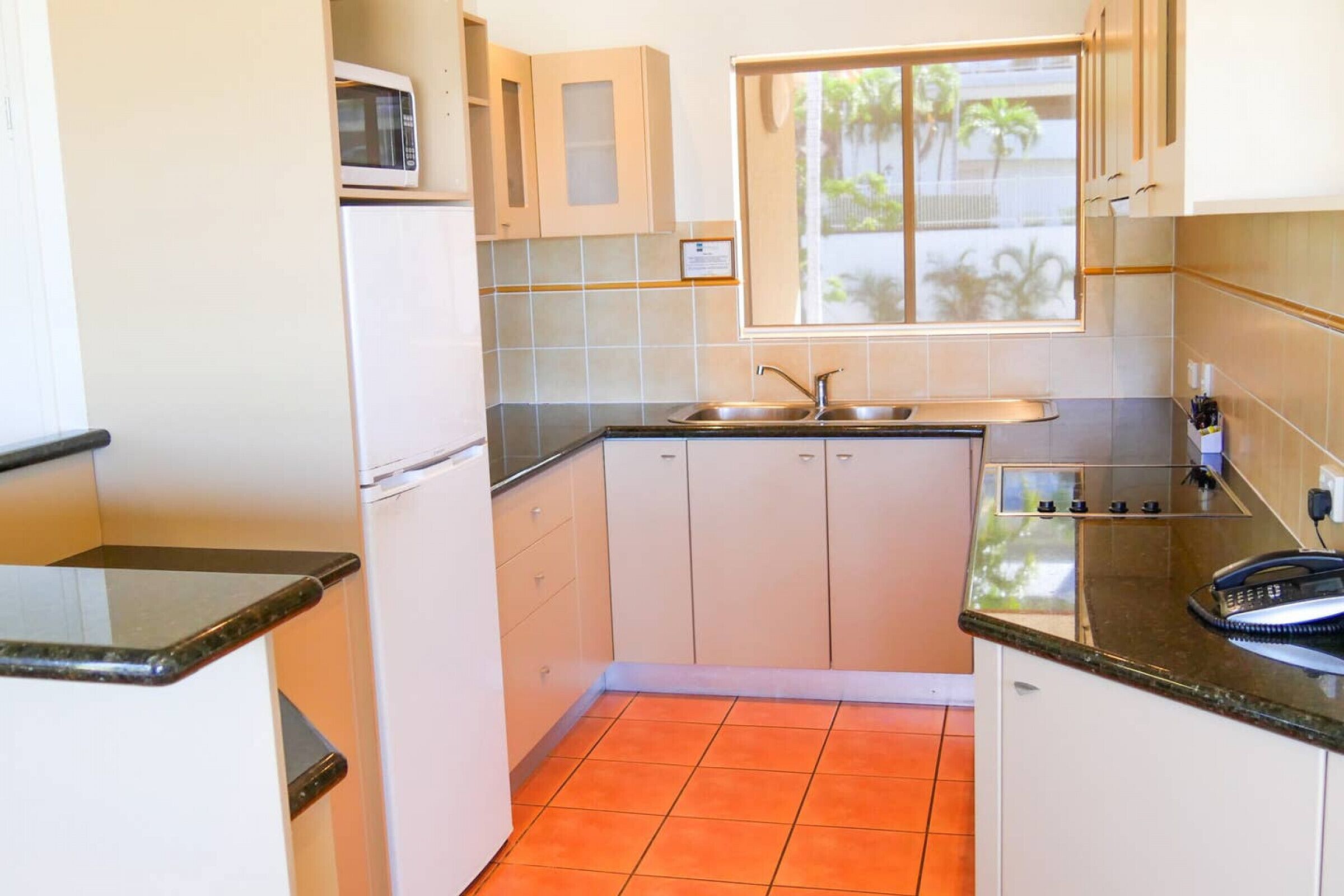 Een kleine keuken met een magnetron, spoelbak en raam.