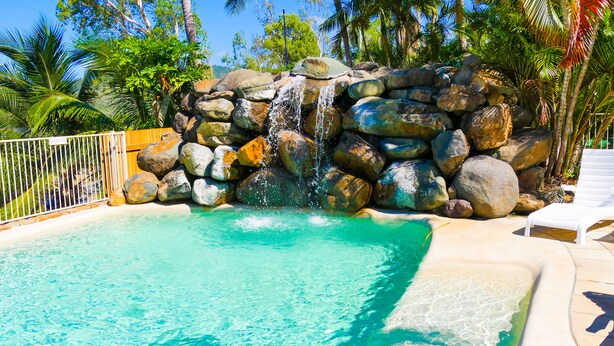 A pool with clear turquoise water, surrounded by large rocks and palm trees. - Spa Haven 17B (Airlie Beach)
