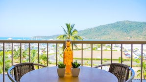 A balcony with a table and chairs, overlooking a marina and a hilly landscape. - Spa Haven 17B (Airlie Beach)