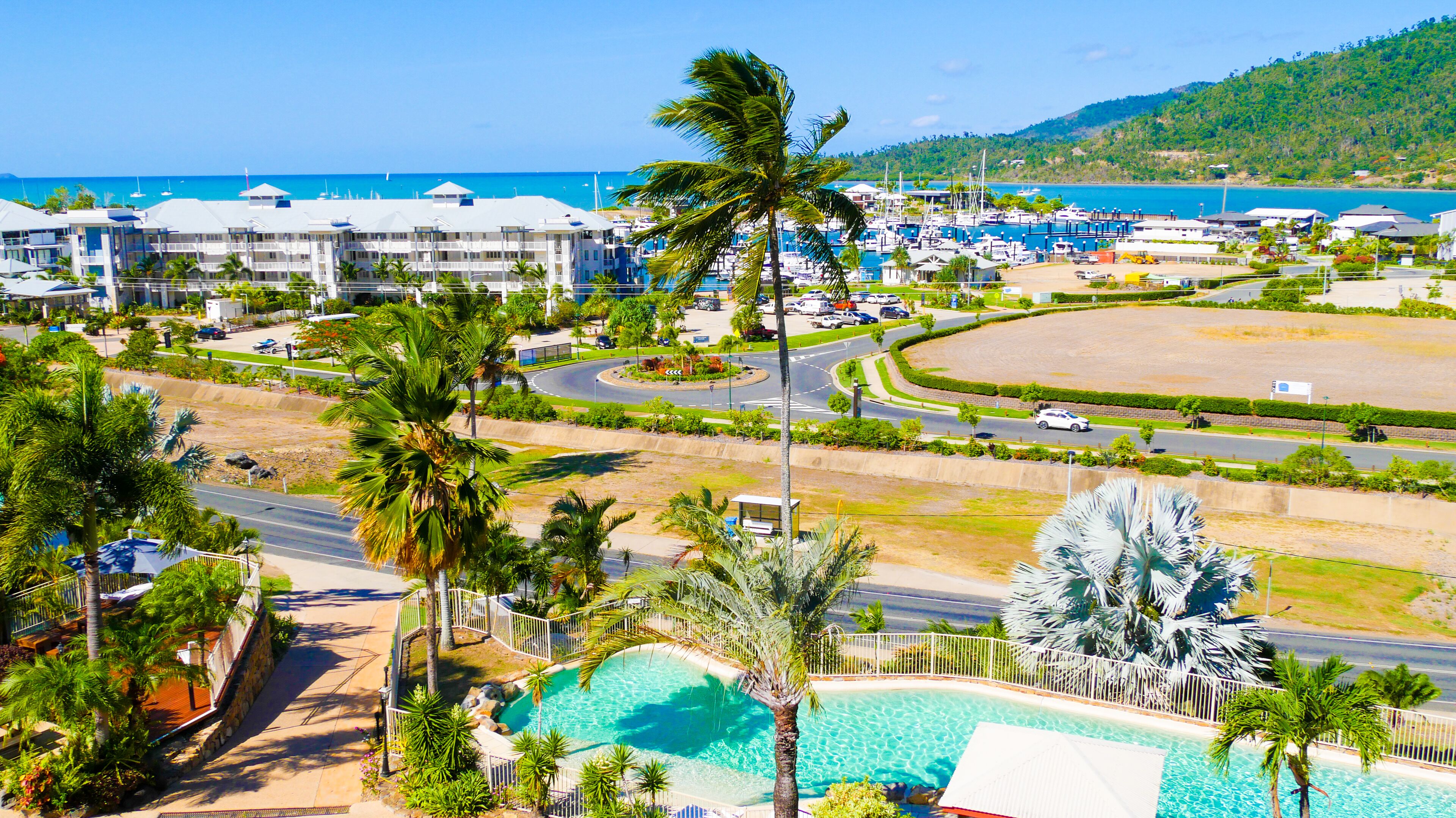 A resort with a swimming pool, palm trees, and a marina with boats.