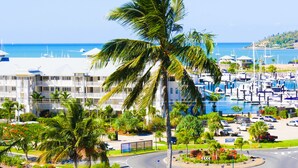 A marina with boats, a hotel with balconies, and palm trees. - Spa Haven 17B (Airlie Beach)