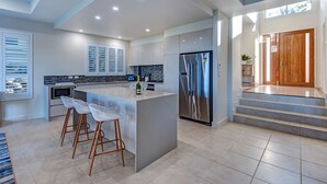 A modern kitchen with a central island, bar stools, a stainless steel refrigerator, and a view of the living area. - La Bella Waters 2 Hamilton Island (Hamilton Island)