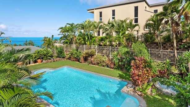 A swimming pool with a view of the ocean, surrounded by lush greenery and a fence. - La Bella Waters 2 Hamilton Island (Hamilton Island)