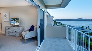 A balcony with a view of the sea and mountains, a sofa, a TV, and a marble cabinet. - La Bella Waters 2 Hamilton Island (Hamilton Island)