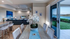 A modern dining area with a large table, white chairs, and a centerpiece of white orchids. - La Bella Waters 2 Hamilton Island (Hamilton Island)