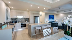 A modern kitchen with a central island, bar stools, and a dining table with chairs. - La Bella Waters 2 Hamilton Island (Hamilton Island)