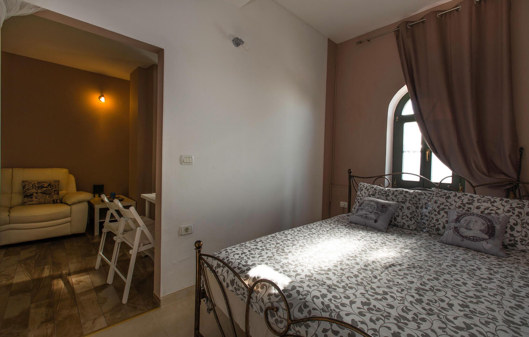 A bedroom with a bed, a chair, a small table, and a window with curtains.