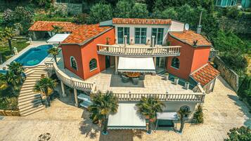 A large, multi-story house with a swimming pool, outdoor seating, and a landscaped garden.