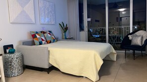 Un dormitorio con una cama, una silla, una mesita y un jarrón con flores.