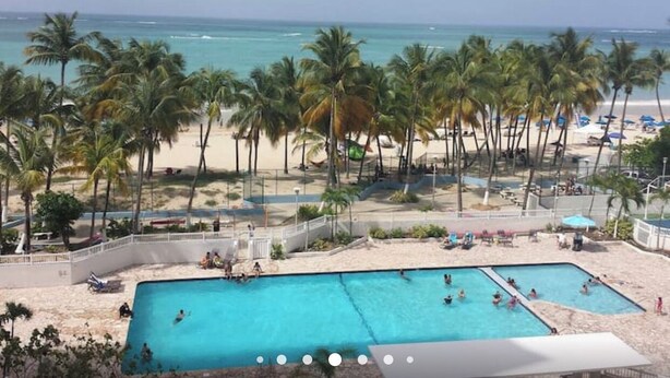 Un resort en la playa con zona de piscina, palmeras y vistas al océano.