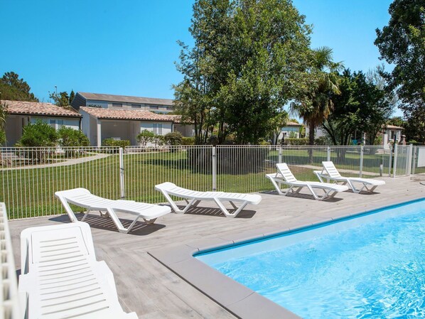 A pool area with white lounge chairs and a clear blue pool.