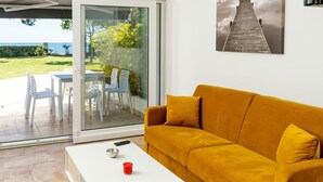 A living room with a yellow sofa, white coffee table, and a glass door leading to an outdoor area with a table and chairs.